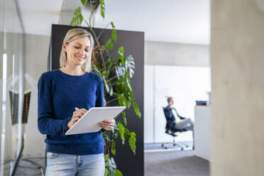 Smiling businesswoman using digital tablet in office - DIGF18056