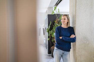 Lächelnde Geschäftsfrau, die sich im Büro an eine Säule lehnt - DIGF18057