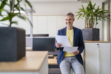Lächelnder Geschäftsmann bei der Arbeit an Papieren im Büro - DIGF18068