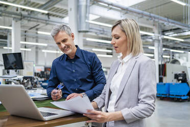 Businessman and businesswoman working on laptop together in factory - DIGF18081