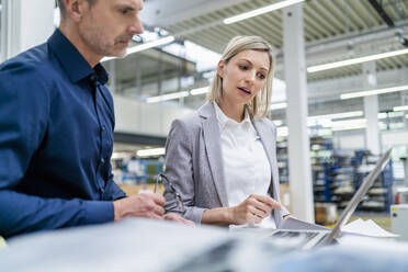 Geschäftsmann und Geschäftsfrau arbeiten zusammen an einem Laptop in einer Fabrik - DIGF18084