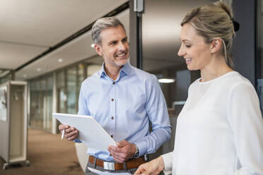 Smiling businessman with digital tablet and businesswoman talking in office - DIGF18092