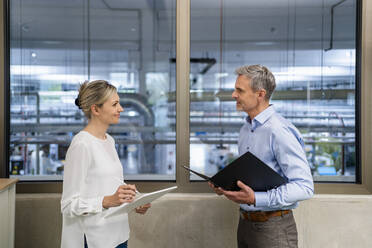 Geschäftsmann mit Klemmbrett und Geschäftsfrau mit digitalem Tablet im Gespräch in der Fabrik Büro - DIGF18099