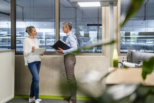 Geschäftsmann mit Klemmbrett und Geschäftsfrau mit digitalem Tablet im Gespräch in der Fabrik Büro - DIGF18102