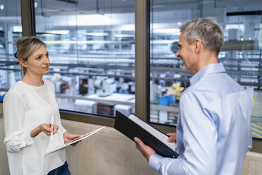 Geschäftsmann mit Klemmbrett und Geschäftsfrau mit digitalem Tablet im Gespräch in der Fabrik Büro - DIGF18105