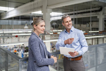 Businessman with digital tablet and businesswoman talking in factory - DIGF18114