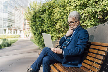 Älterer Geschäftsmann mit Laptop auf einer Bank im Büropark sitzend - MEUF06238