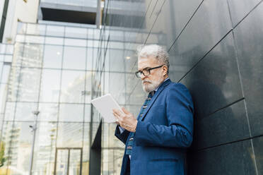 Senior businessman using tablet PC outside office building - MEUF06247