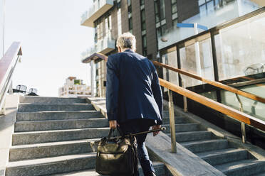 Senior businessman walking up steps outside office building on sunny day - MEUF06269