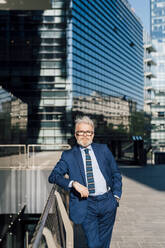 Älterer Geschäftsmann steht an einem Geländer vor einem Bürogebäude - MEUF06280