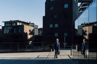 Älterer Geschäftsmann steht vor einem Bürogebäude an einem sonnigen Tag - MEUF06315