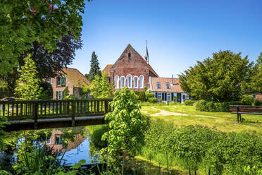 Deutschland, Niedersachsen, Krummhorn, Kleine Brücke über stehendes Wasser mit Loquard-Kirche im Hintergrund - PUF01999