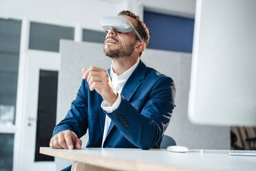 Geschäftsmann mit Virtual-Reality-Headset sitzt am Schreibtisch im Büro - MOEF04137