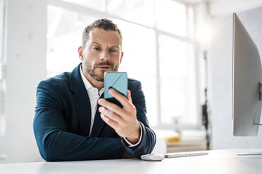 Lächelnder Geschäftsmann schaut auf sein Smartphone im Büro - MOEF04142