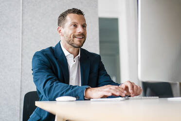 Lächelnder arbeitender Mann, der einen Desktop-PC am Schreibtisch im Büro benutzt - MOEF04145