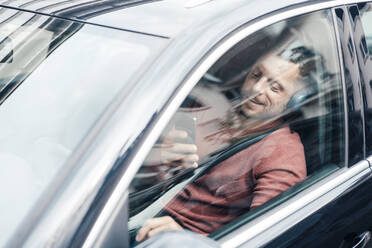 Smiling man using smart phone sitting in car - MOEF04150