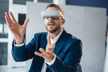 Businessman gesturing wearing virtual reality headset in office - MOEF04164