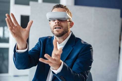 Geschäftsmann gestikuliert mit Virtual-Reality-Headset im Büro - MOEF04164
