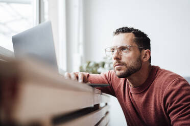 Freiberufler mit Brille arbeitet zu Hause am Laptop - MOEF04178