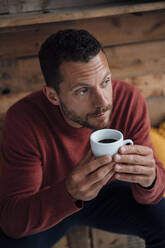 Contemplated man with coffee cup sitting on bench - MOEF04180