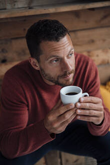 Nachdenklicher Mann mit Kaffeetasse auf einer Bank sitzend - MOEF04180