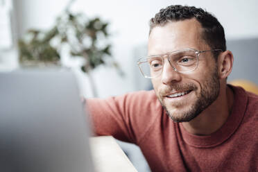 Smiling freelancer with eyeglasses looking at laptop - MOEF04182