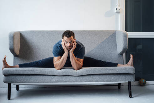 Gelangweilter Mann mit ausgestreckten Beinen sitzt zu Hause auf dem Sofa - MOEF04205