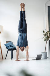 Mann macht Handstand auf einem Stuhl vor einer Wand zu Hause - MOEF04217