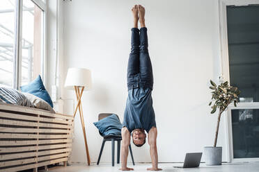 Man practicing handstand in front of wall at home - MOEF04219