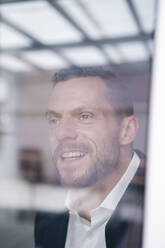Mature businessman smiling seen through window - MOEF04230