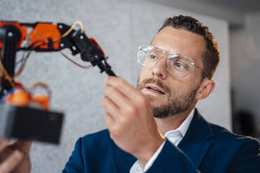 Technician wearing eyeglasses examining robotic model in office - MOEF04231