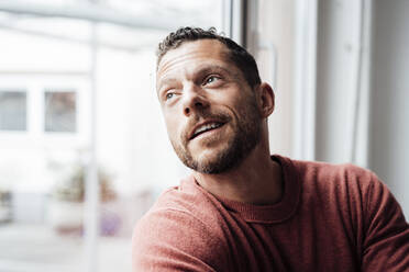 Smiling mature man looking out of window at home - MOEF04244