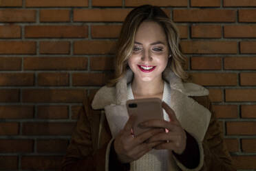 Lächelnde Frau mit Mobiltelefon vor einer Wand - WPEF05972
