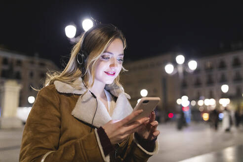 Frau mit Smartphone hört Musik über Kopfhörer in der Stadt - WPEF05980