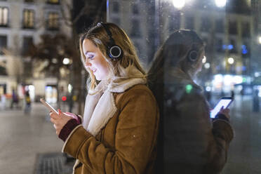 Frau, die ein Mobiltelefon benutzt und sich an eine Glaswand lehnt - WPEF05981