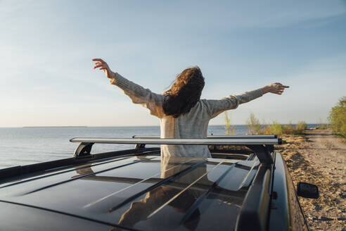 Junge Frau steht mit ausgestreckten Armen auf dem Sonnendach eines Autos - VPIF06348