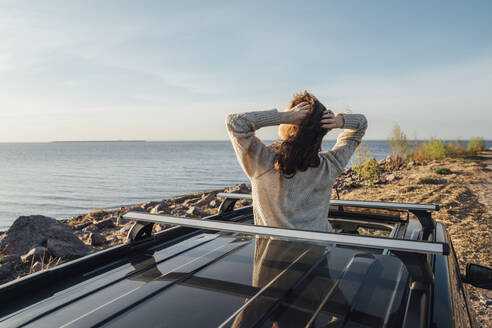 Junge Frau mit Händen hinter dem Kopf genießt Brise durch Sonnendach des Autos - VPIF06349