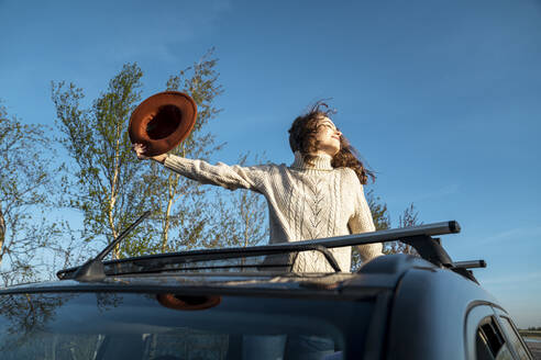 Glückliche Frau mit Hut, die das Sonnenlicht durch das Sonnendach eines Autos genießt - VPIF06351