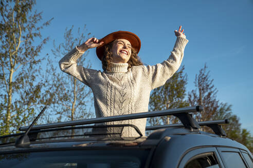 Fröhliche Frau mit Hut, die durch das Sonnendach eines Autos genießt - VPIF06353
