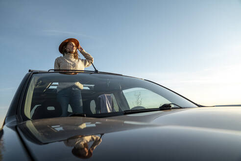Lächelnde Frau mit Hut im Auto stehend durch das Sonnendach - VPIF06356