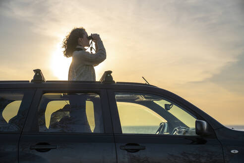 Junge Frau schaut bei Sonnenuntergang durch ein Fernglas - VPIF06363
