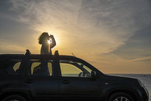 Frau schaut bei Sonnenuntergang durch ein Fernglas - VPIF06364