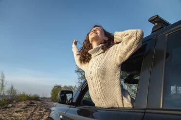 Happy woman leaning out of car window on sunny day - VPIF06374