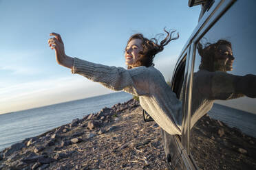 Happy young woman with eyes closed leaning out of car window - VPIF06375