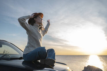 Young woman wearing hat sitting on car hood - VPIF06380