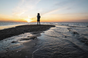 Junge Frau mit Rucksack steht am Meer bei Sonnenuntergang - VPIF06409