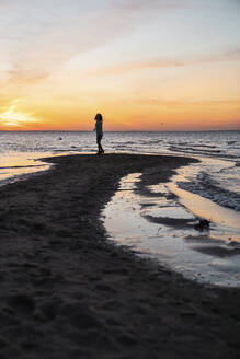 Junge Frau steht bei Sonnenuntergang am Meer - VPIF06416