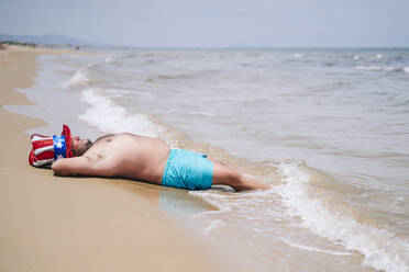Sorgloser Mann ohne Hemd und mit Onkel-Sam-Hut entspannt sich am Strand - OCMF02449