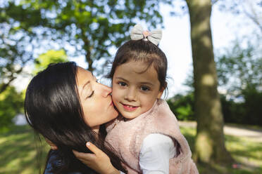 Mother kissing daughter in park on sunny day - IHF00885