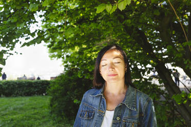 Frau mit Jeansjacke und geschlossenen Augen im Park - IHF00891